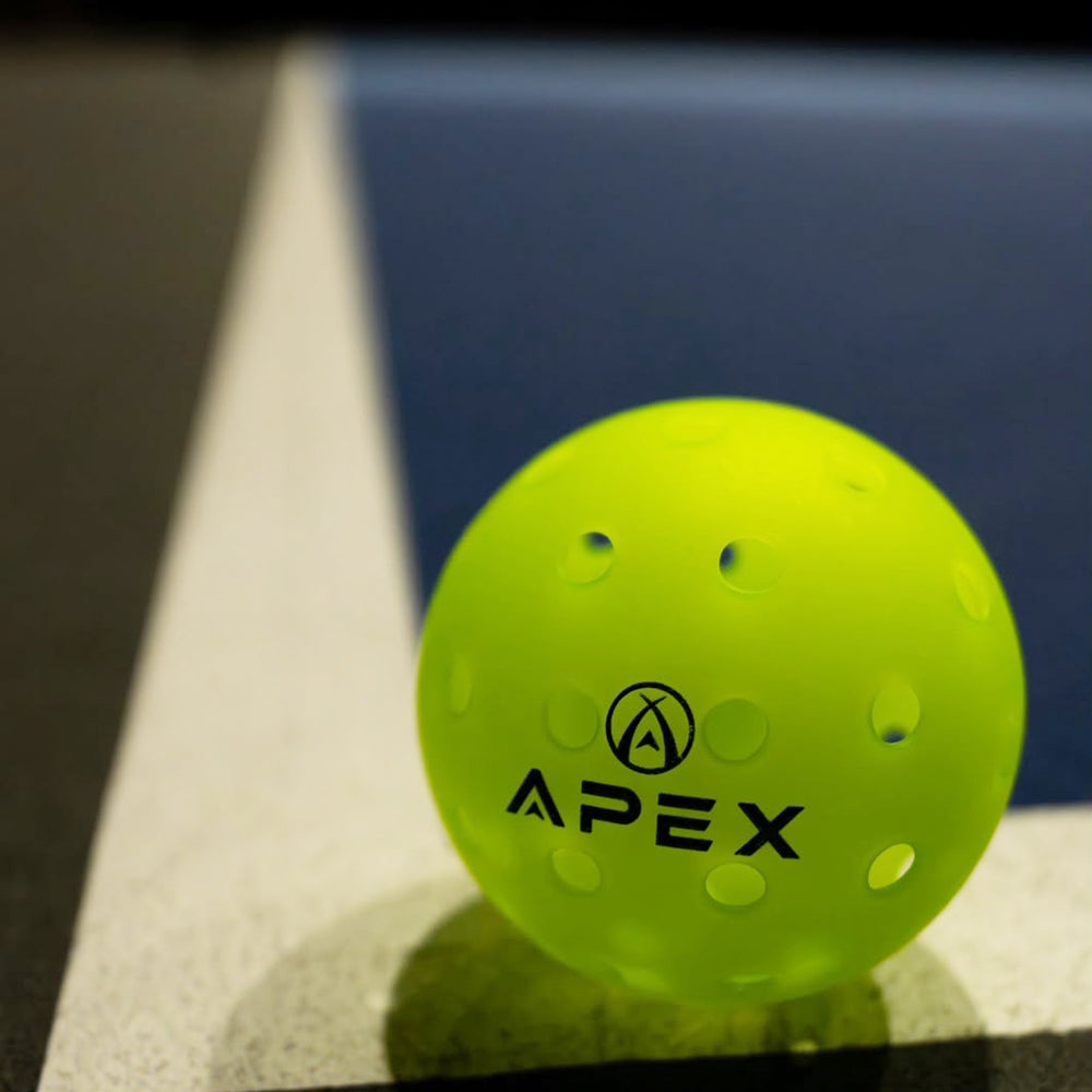 Three APEX pickleballs resting on a court line